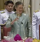 Photograph of an old lady proposing a toast with her right hand.
