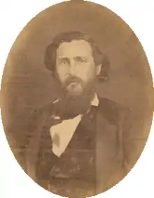 Sepia tone photo shows a bearded man in a black coat.