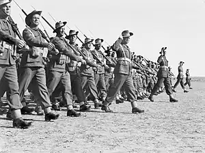 Black and white photo of a large group of men wearing military uniforms and carrying rifles marching in close formation