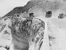 A road at the edge of a cliff with trucks driving both ways along it.