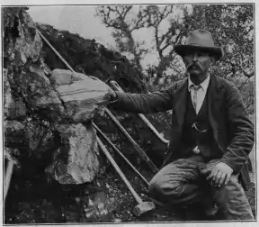 William E. Hidden next to a 73 lb (33 kg) mass of gadolinite in place at Barringer Hill, 1903.