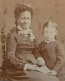Photograph of a dark-skinned woman in a Victorian-era dress seated next to a standing child