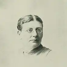 Portrait photo of a middle-aged woman wearing glasses with an up-do hairstyle parted in the center.