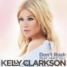 An image of a blonde looking aside against a pinkish background. A blue shirt is draped around her shoulder. Below her, the words "Don't Rush feat. Vince Gill" is written in grey color. Below these words, the word "Kelly Clarkson" is written in black capital letters.