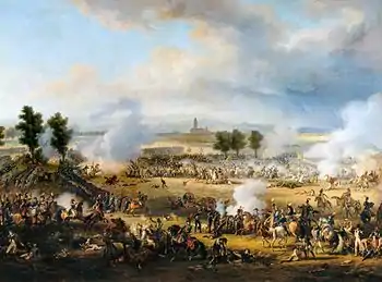 A crowded scene with many soldiers and horses, and much smoke. Some soldiers lie dead or wounded. In the distance, beyond a short line of trees, is a tall church tower.