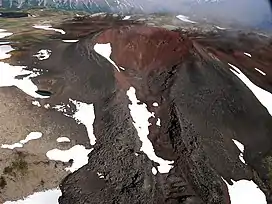 A dark-coloured volcanic cone rising above a sparsely snow-covered plateau.