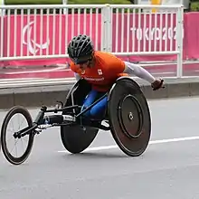 Woman with orange top racing in a black wheelchair.