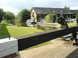 A canal lock in the sunshine. Behind the lock is a Victorian brick building, formerly a pumping station, now a private residence.