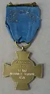 Back of a bronze cross-shaped medal hanging from a blue ribbon